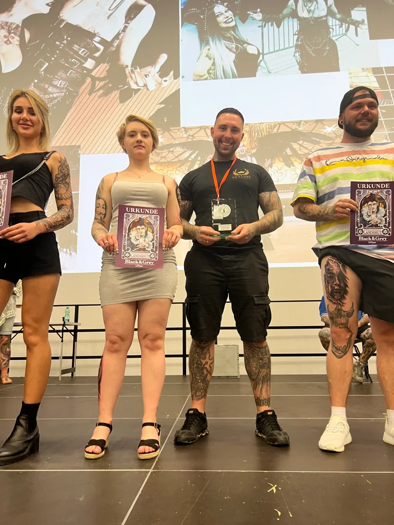 Der Besitzer von Skyline Tattoo posiert mit dem Mädchen, das er tätowiert hat. Sie hält die Urkunde in der Hand, er den Preis für den ersten Platz. Nummer eins an diesem Wochenende in Landshut, Bayern.