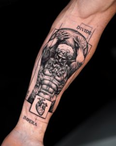 Tätowierung, die einen Mann darstellt, der an eine Statue erinnert und eine Last auf seinen Schultern trägt. Unter ihm ein Herz und die Aufschrift „Divide et impera” (Teile und herrsche).