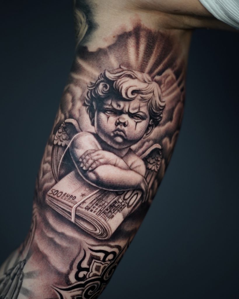 Realistisches Chicano Engel Tattoo am inneren Oberarm mit verschränkten Armen und Geldschein, detailreiche Schattierungen im Black & Grey Stil, ausdrucksstarkes Motiv mit ernster Mimik und symbolischer Bedeutung für Schutz, Stärke und Erfolg - gestochen bei Skyline Tattoo