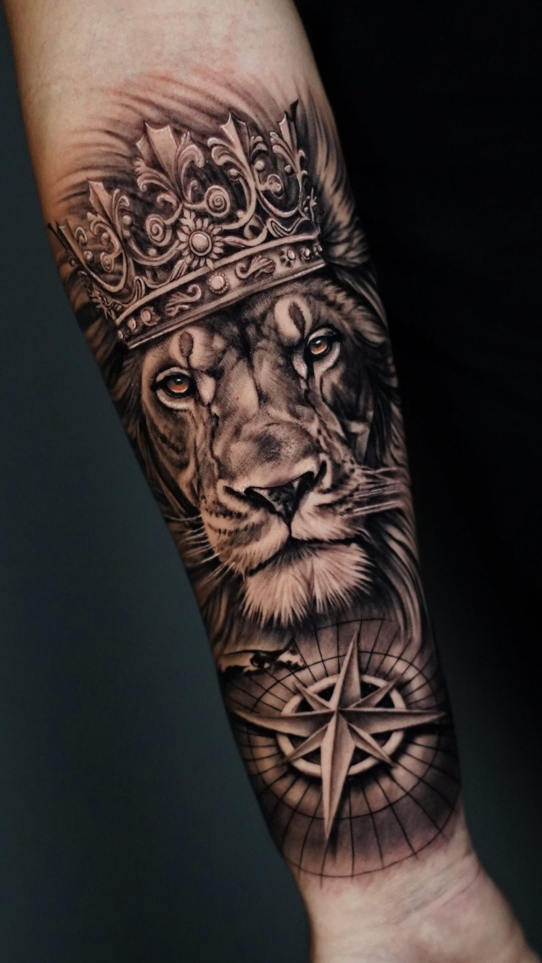 Realistisches Unterarm Tattoo eines Löwen mit detailreicher Krone auf dem Kopf und intensivem Blick, kombiniert mit einem Kompass als Symbol für Orientierung und Lebensweg, gestochen im Black & Grey Realismus Stil mit feinen Schattierungen und starken Kontrasten, kraftvolles Motiv für Stärke, Führung und Selbstbestimmung - gestochen bei Skyline Tattoo von Josef Skoric in Rohrbach