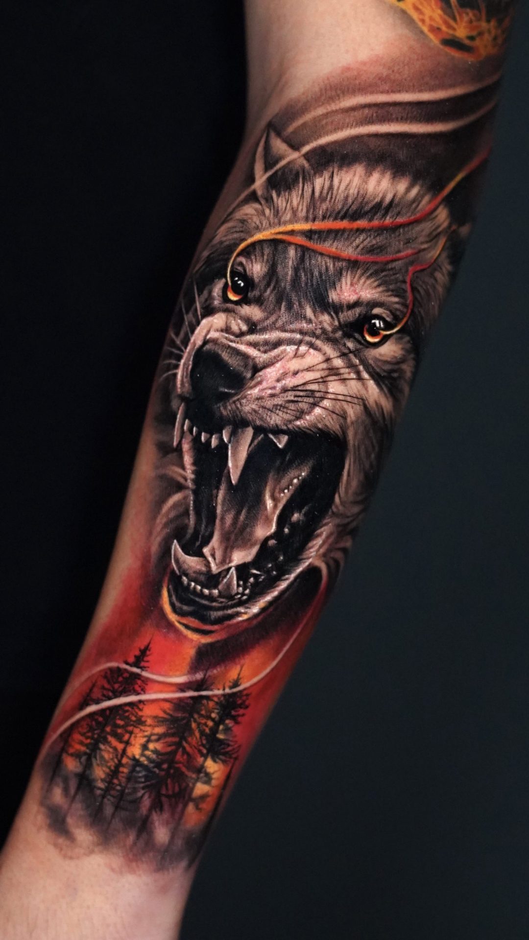 Tätowierung, die einen Wolf darstellt, unter ihm Bäume und die Farben des Sonnenuntergangs.
