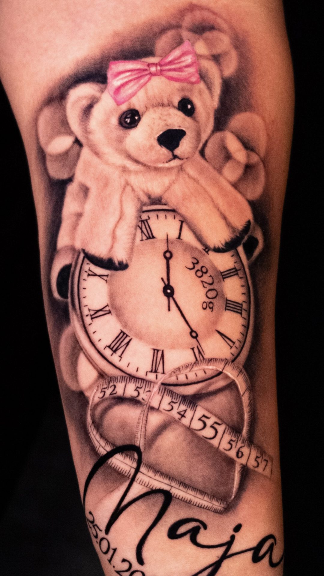 Tätowierung, die eine Uhr mit der Aufschrift „3820g“ darstellt, darüber ein Plüschtier, darunter ein Maßband, der Name „Maja“ und ein Datum.