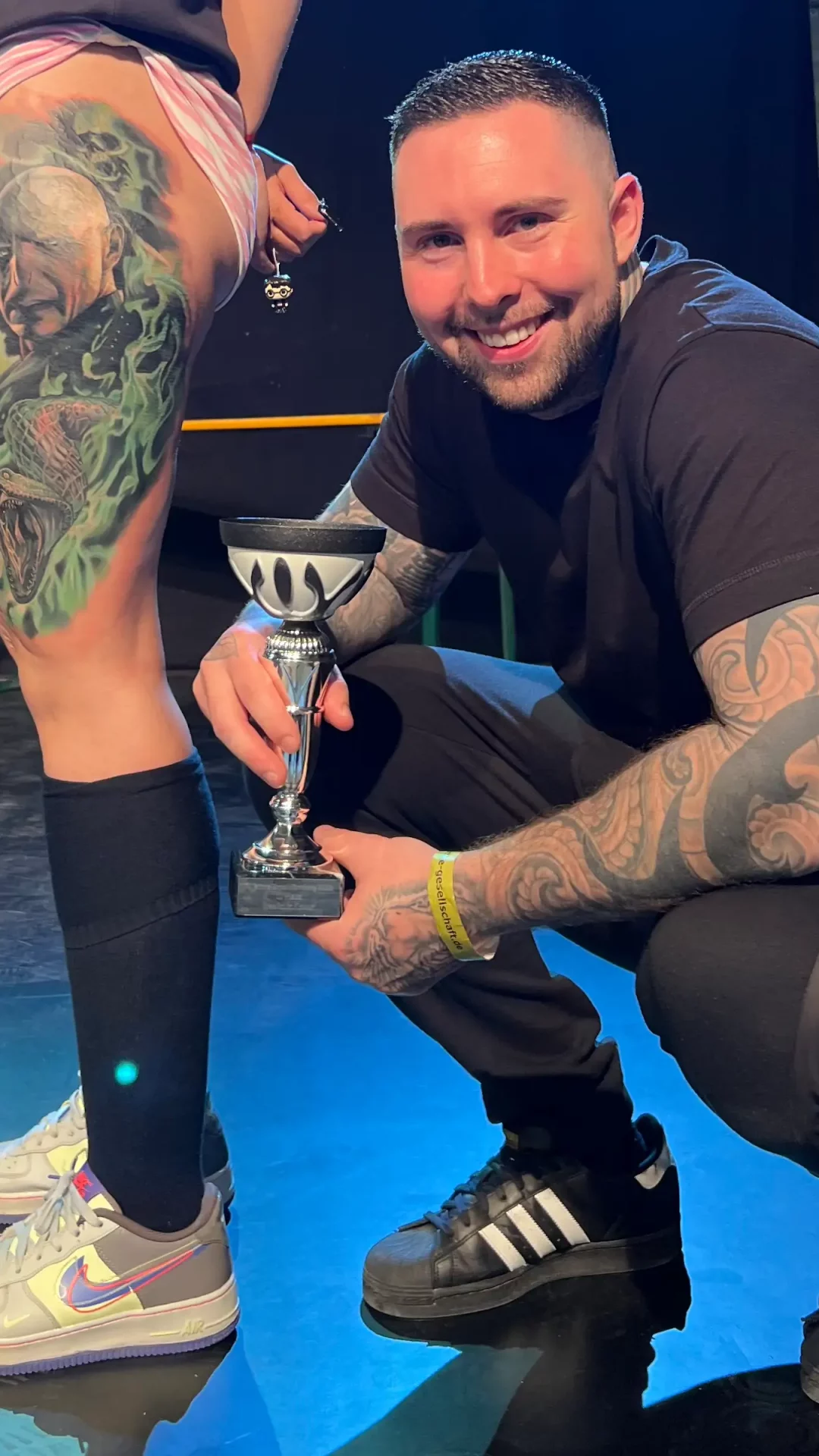 Der Besitzer von Skyline Tattoo posiert mit dem Mädchen, das er tätowiert hat. Er hält den Pokal für den ersten Platz in den Händen.